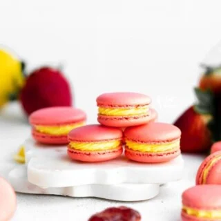 Pink Strawberry Lemon Macarons filled with yellow lemon buttercream are stacked on a small white marble board