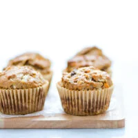 baked gluten free morning glory muffins in brown paper liners on a small light colored wood cutting board
