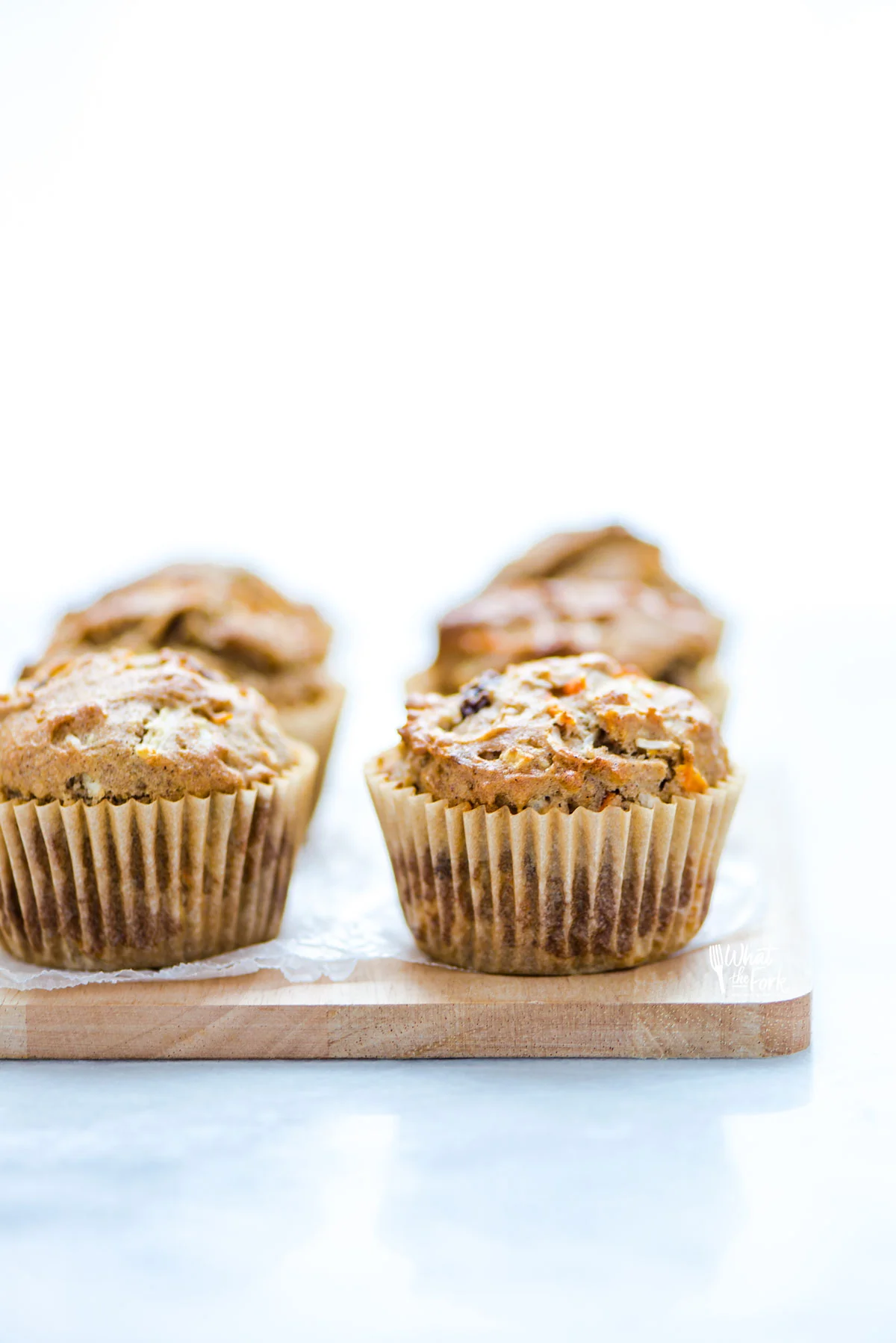 baked gluten free morning glory muffins in brown paper liners on a small light colored wood cutting board