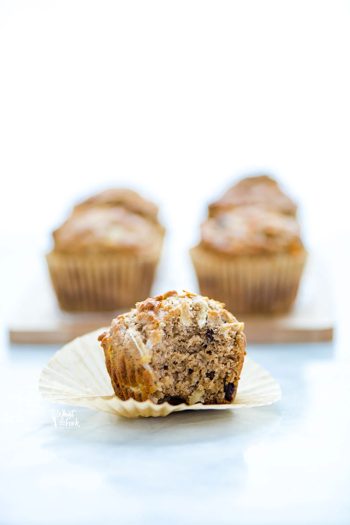 a gluten free morning glory muffin unwrapped an on top of a brown paper liner with a bite taken out of the muffin