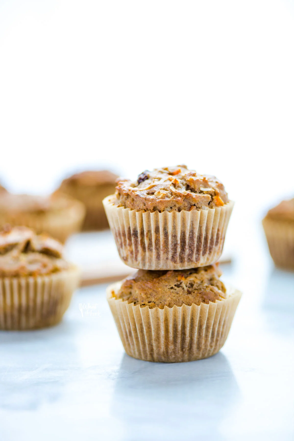 2 gluten free morning glory muffins in brown paper liners stacked on top of each other with more muffins in the background