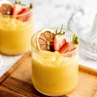 finished lemon pudding recipe served in a clear glass with ridges topped with a charred lemon wheel and a fresh strawberry cut in half