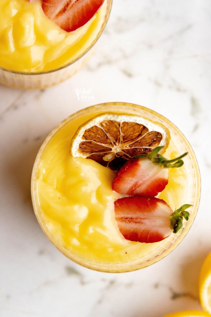 overhead shot of lemon pudding in a glass topped with a charred lemon wheel and a fresh strawberry cut in half