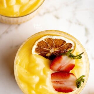 overhead shot of lemon pudding in a glass topped with a charred lemon wheel and a fresh strawberry cut in half