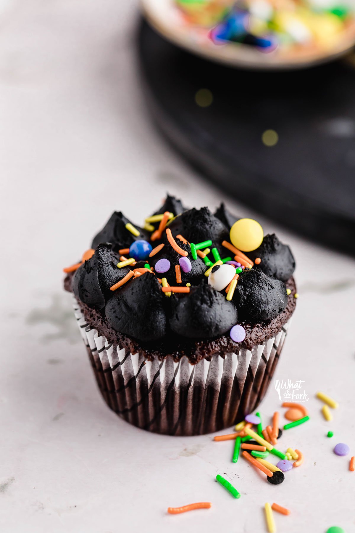 Black Frosting Recipe (American Buttercream) on a chocolate cupcake in a white paper liner decorated with Halloween sprinkles