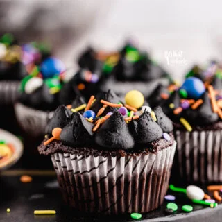 Black Frosting Recipe (American Buttercream) used to decorate chocolate cupcakes in white paper liners garnished with Halloween color sprinkles