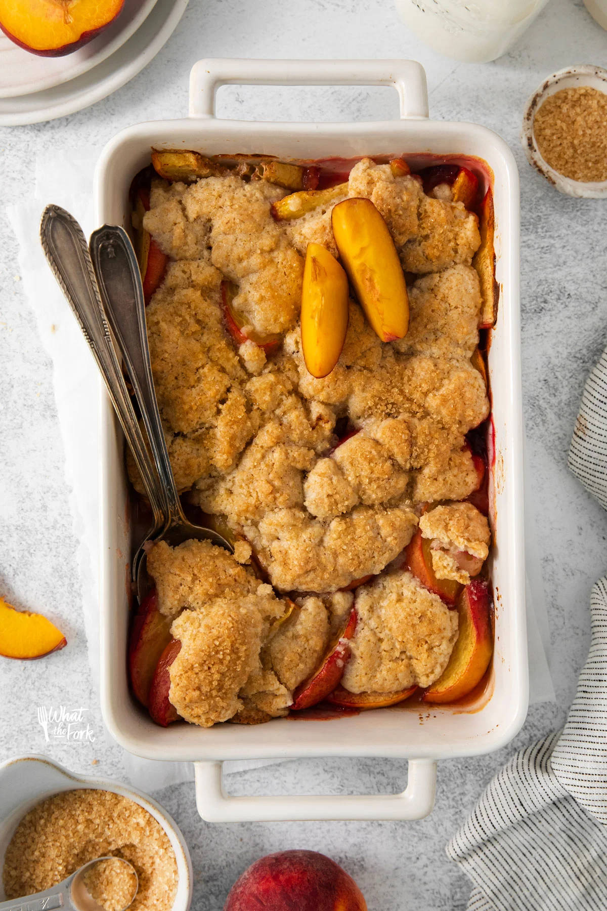 overhead shot of a baked gluten free peach cobbler recipe in a white rectangle baking dish with a serving spoon in it ready to serve