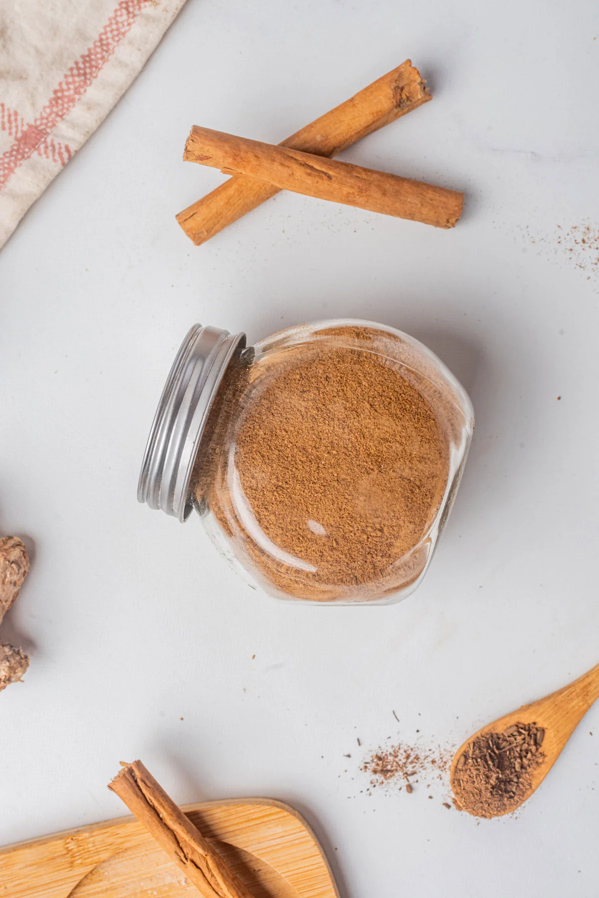 homemade pumpkin pie spice in a glass jar with a metal screw top lid on a white surface with cinnamon sticks nearby