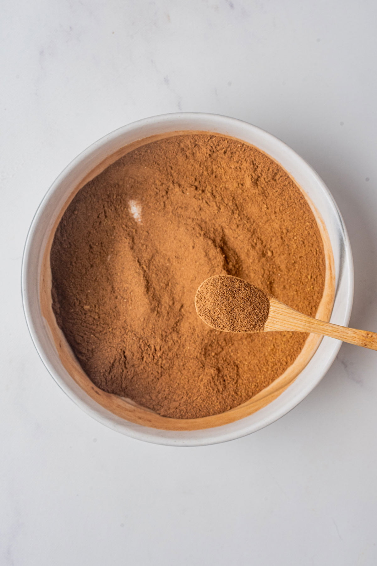 Homemade Pumpkin Pie Spice (Easy DIY Recipe) mixed together in a small white bowl with a small wood spoonful held above the bowl