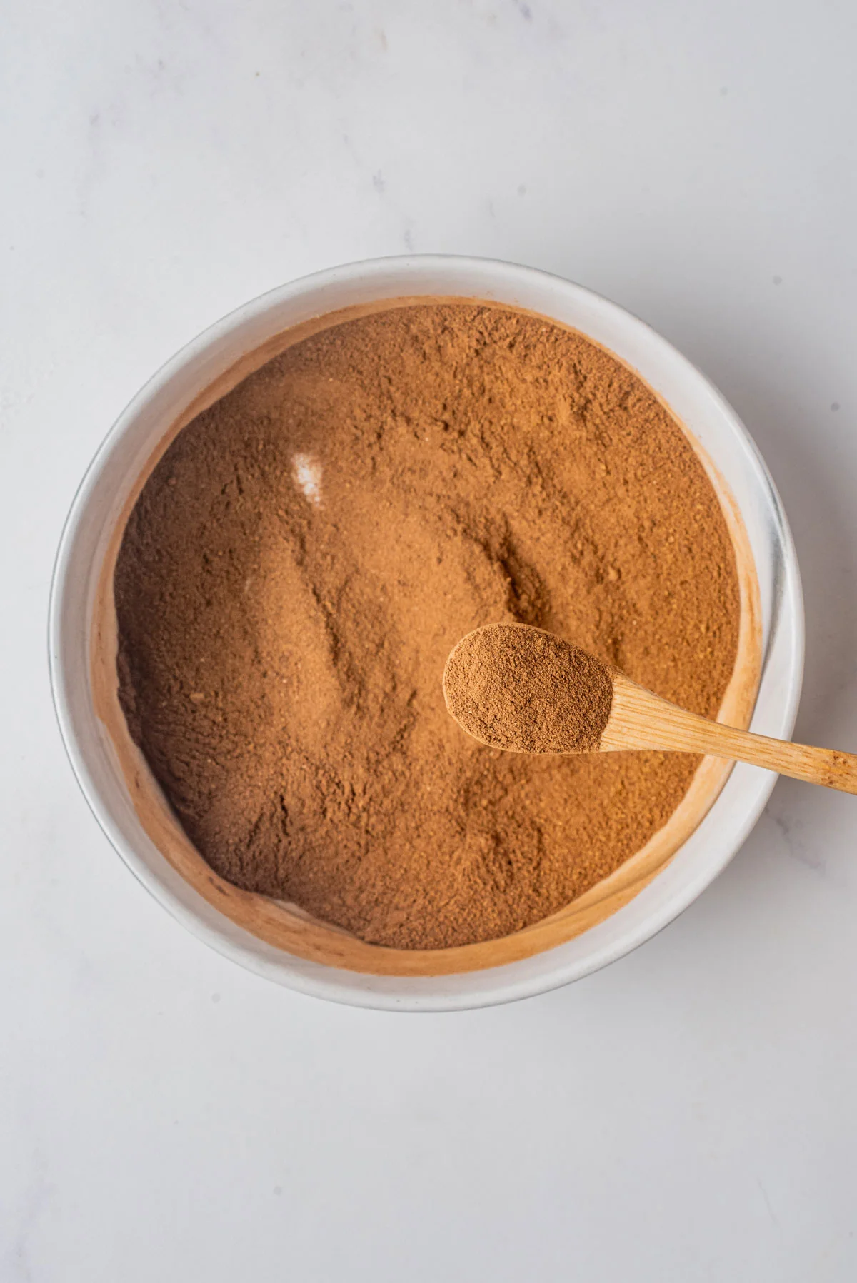 Homemade Pumpkin Pie Spice (Easy DIY Recipe) mixed together in a small white bowl with a small wood spoonful held above the bowl