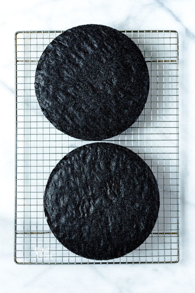 2 layers of gluten free black velvet cake cooling on a metal wire rack on top of a marble surface
