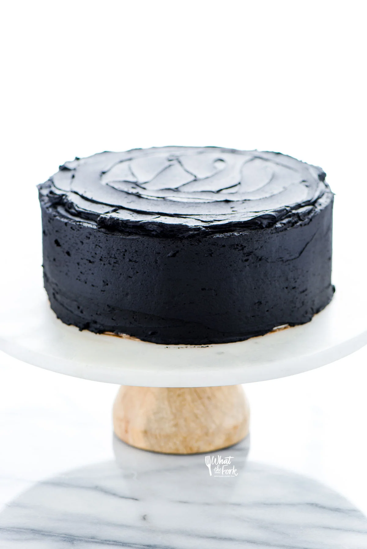 a gluten free black velvet cake frosted with black buttercream on a white marble cake stand with a wood base