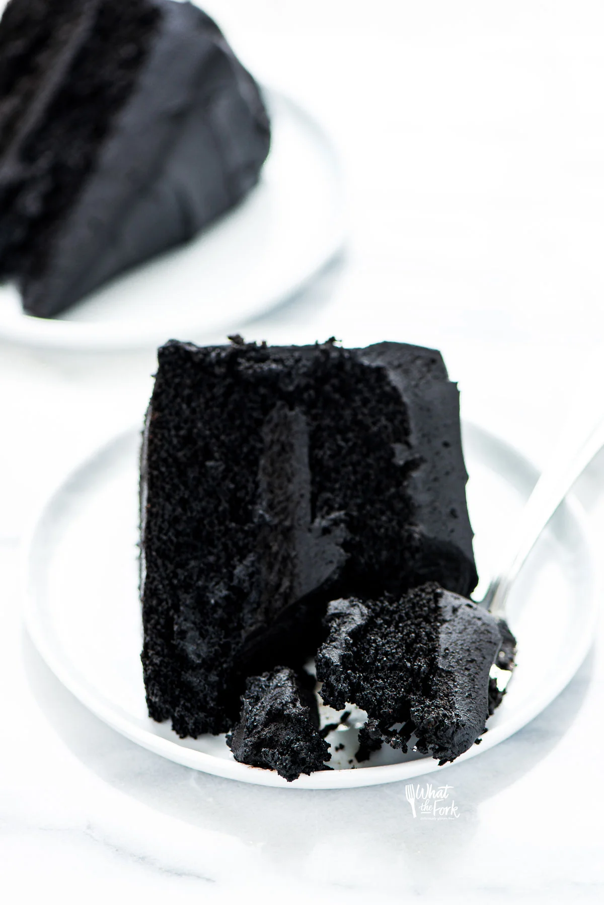 a slice of gluten free black velvet cake on a small white plate with a forkful of cake