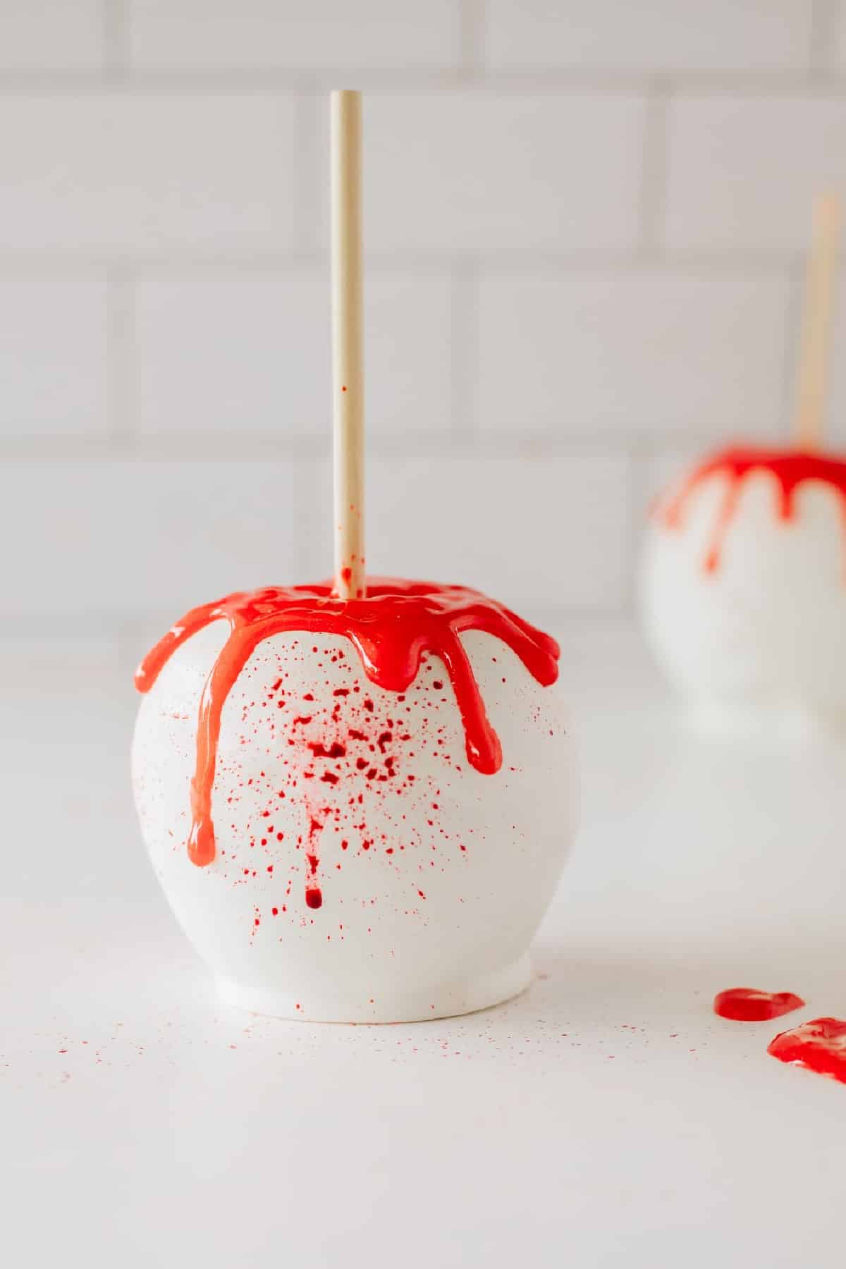A granny smith apple with a dipping stick dipped in white chocolate and splattered with red edible blood. 
