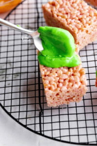 melted green candy melts being spooned onto gluten free rice krispies treats to make Monster Halloween Rice Krispie Treats