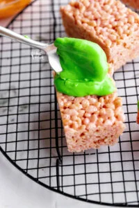 melted green candy melts being spooned onto gluten free rice krispies treats to make Monster Halloween Rice Krispie Treats