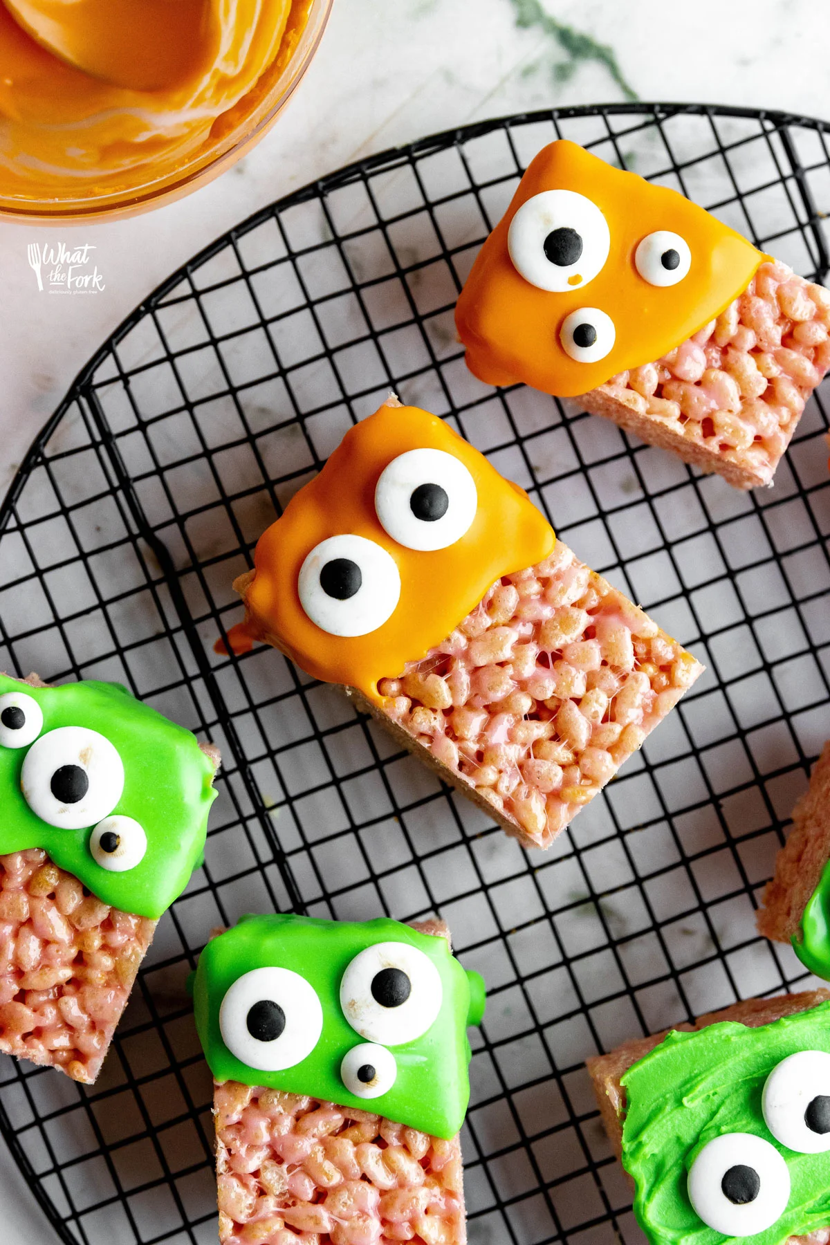 Monster Halloween Rice Krispie Treats on a round black wire rack dipped in orange and green candy melts and decorated with different sized candy eyes