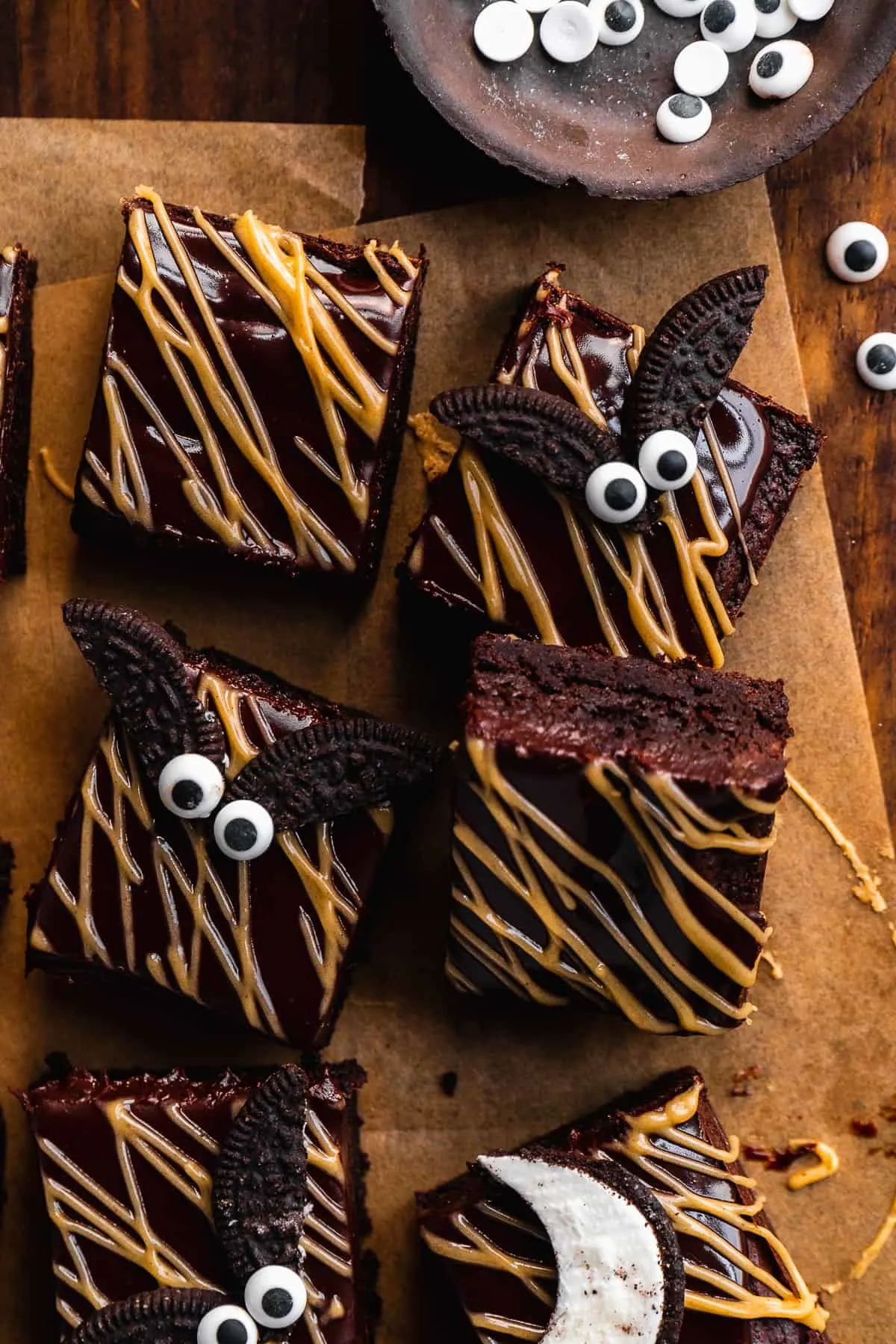 gluten free bat brownies decorated with candy eyes and gluten free Oreo cookies on brown parchment paper on top of a brown wood cutting board