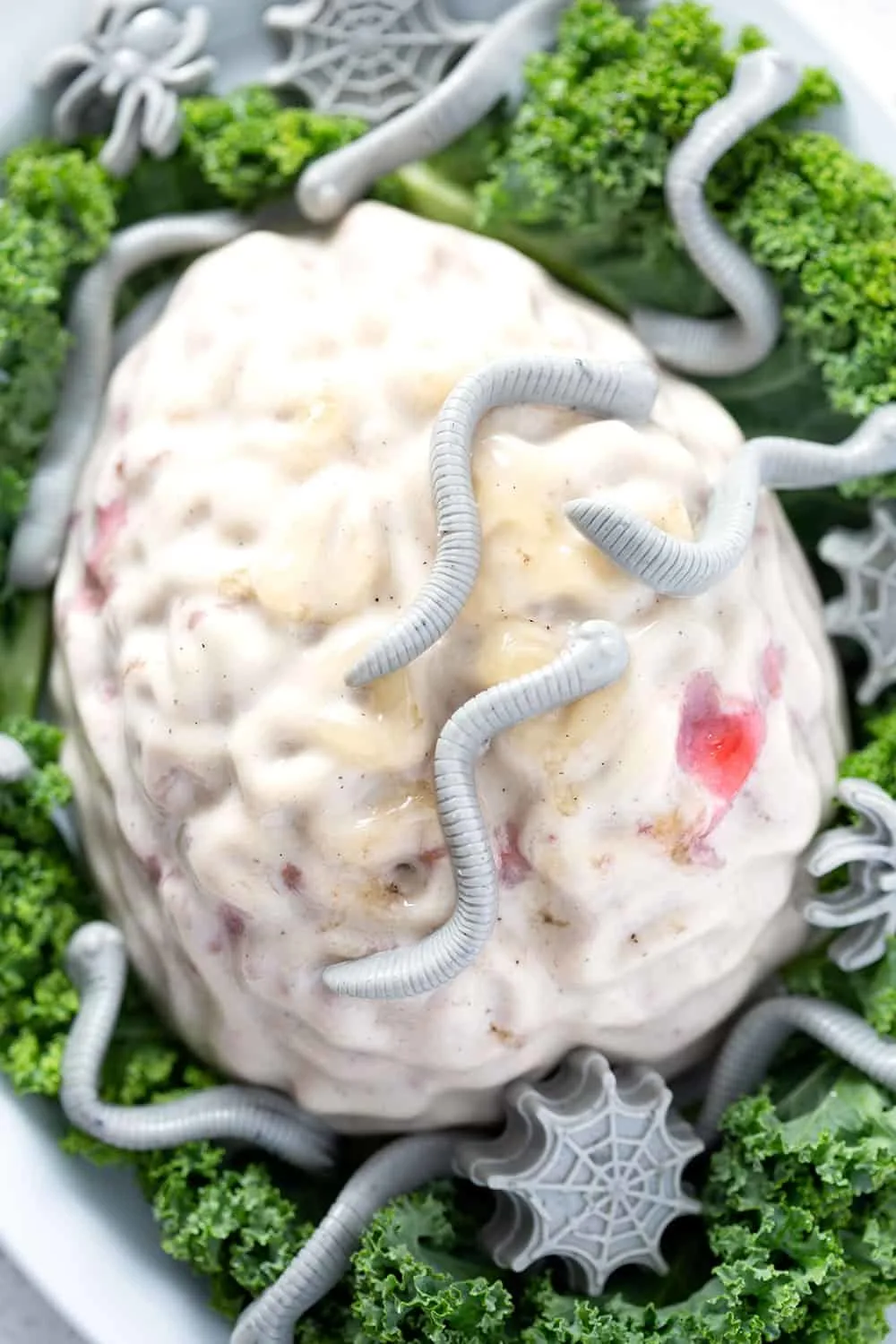 this zombie brain dessert is made with coconut panna cotta and swirls of strawberry jam in a brain mold. It's plated on decorative greens with gray gummy worms and spiders.