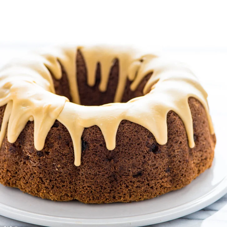 a baked gluten free apple cake topped with maple glaze on a flat white cake plate