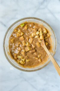 apples stirred into gluten free apple cake batter with a a wood spoon