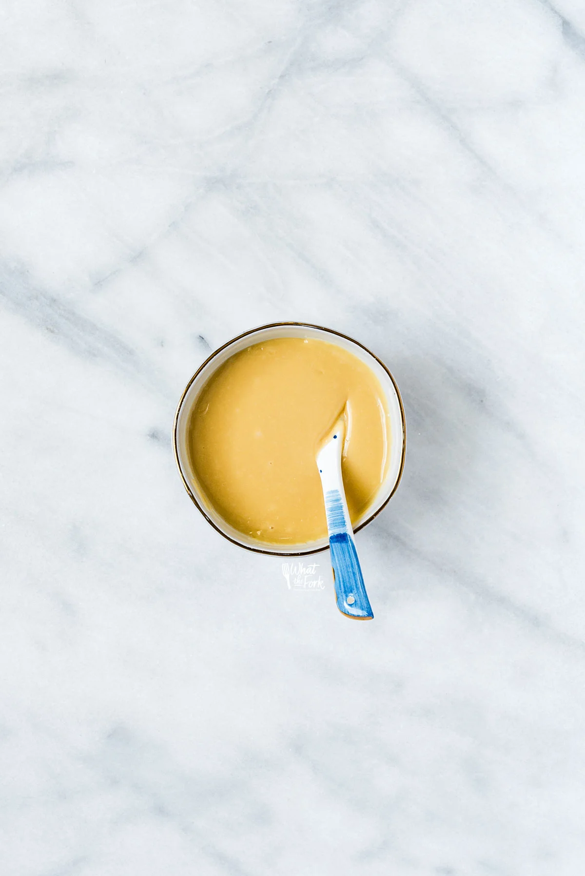 maple glaze in a white bowl with a gold rim with a white and blue spoon in it