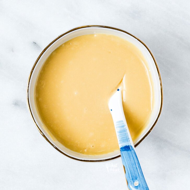 maple glaze in a small white bowl with a gold rim with a white and blue spoon in it