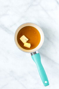 pure maple syrup with two tablespoons of solid butter in a small white saucepan with a aqua blue handle to make maple glaze