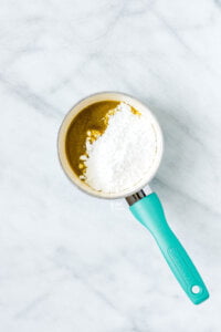 maple syrup with melted butter and powdered sugar on top in a small white saucepan with a aqua blue handle