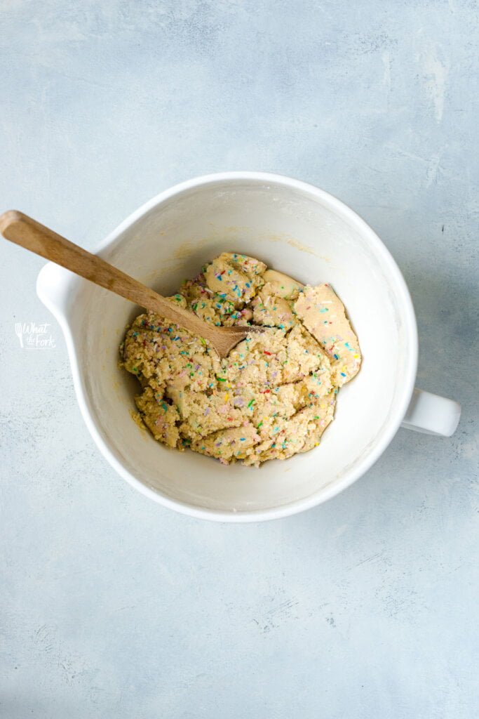 gluten free sugar cookie dough with sprinkles in a white stand mixer bowl with a wood spoon