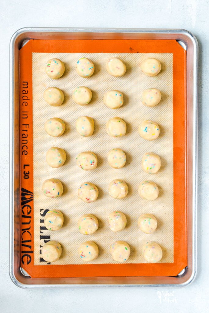 gluten free sugar cookie dough with sprinkles formed into cylinders on a silpat lined half sheet pan.