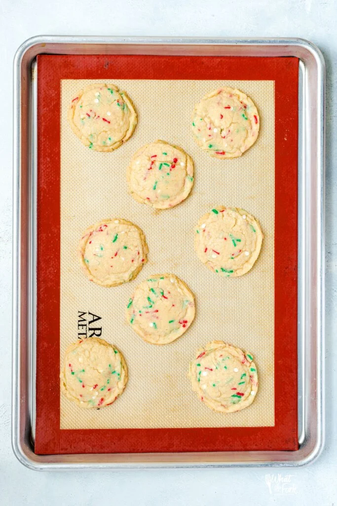 baked gluten free sugar cookies with sprinkles on a half sheet pan lined with a silicone baking mat.