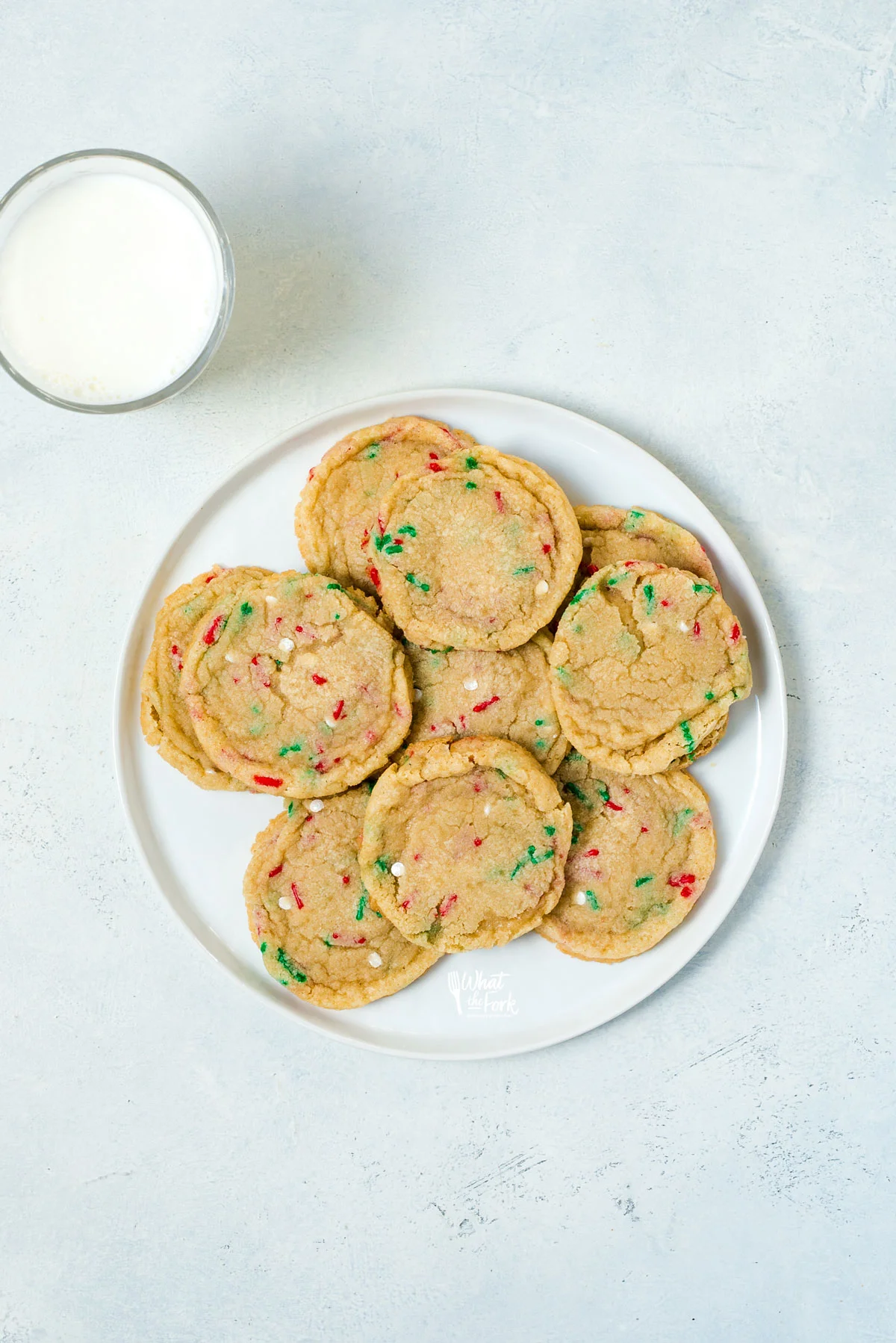 Chewy gluten free sugar cookies made with red and green Christmas sprinkles on a round white plate with a glass of milk next to it
