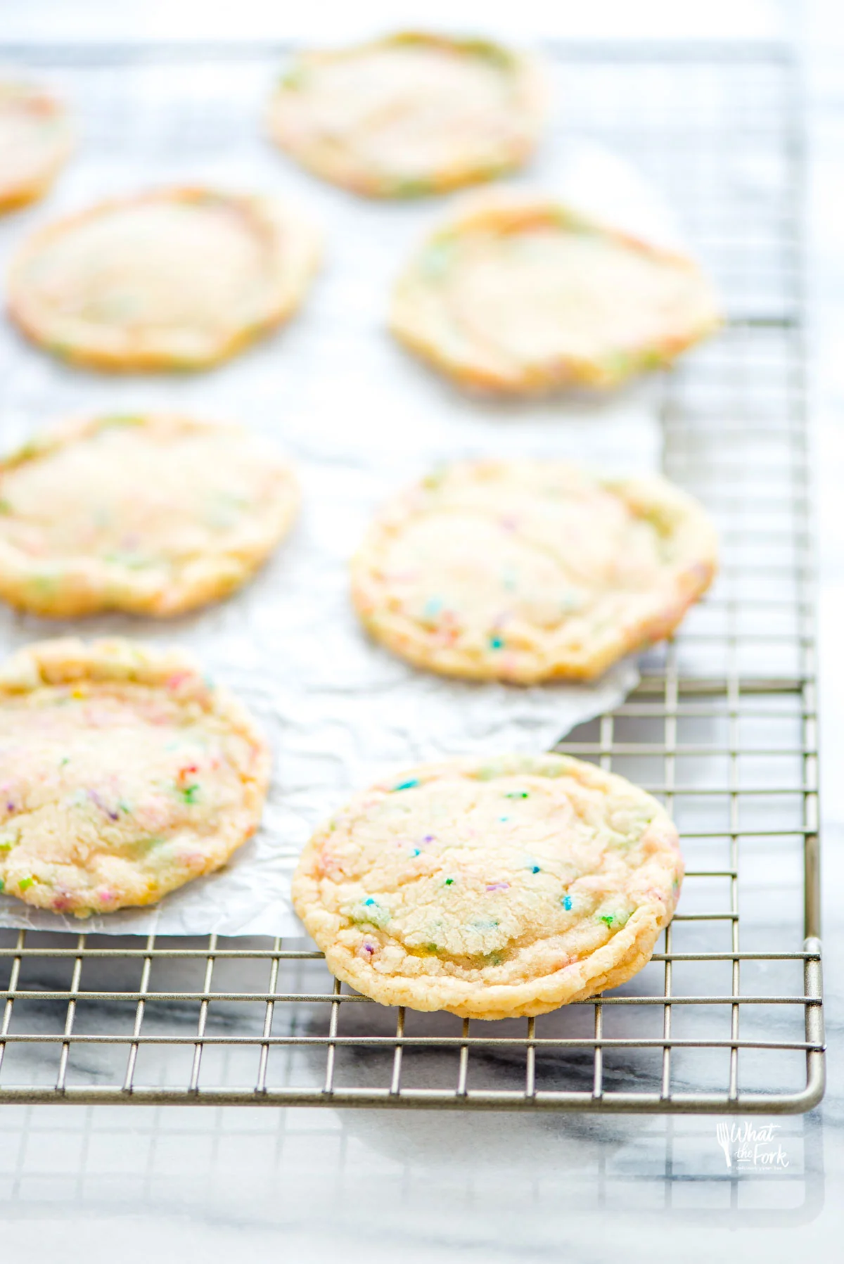 baked chewy gluten free sugar cookies on a wire rack with a small piece of white parchment paper under the cookies.