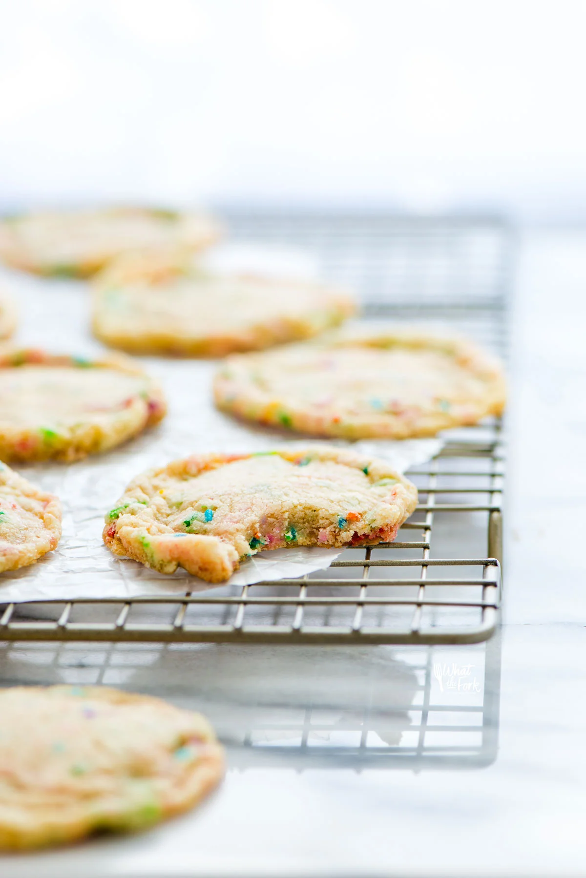 chewy gluten free sugar cookies with sprinkles on a parchment paper lined cooling rack - one cookie has a bite taken out