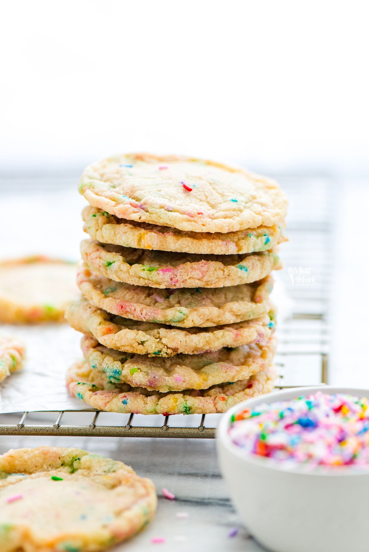 a stack of 7 chewy gluten free sugar cookies on the corner of a wire cooling rack with a small bowl of rainbow sprinkles in the foreground 