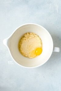 creamed butter and sugar in a white stand mixer bowl with a raw egg and clear vanilla extract on top