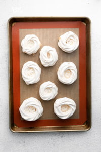 8 baked mini pavlovas on a half sheet pan lined with a silicone baking mat.