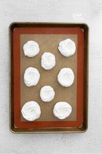 Meringue piped onto a half sheet pan lined with a silicone baking mat to make mini Nutella pavlovas