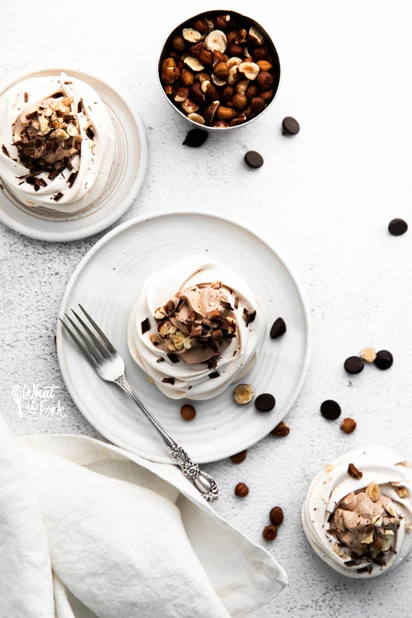 overhead shot of Nutella Pavlovas on small round white plates garnished with chopped hazelnuts and chocolate