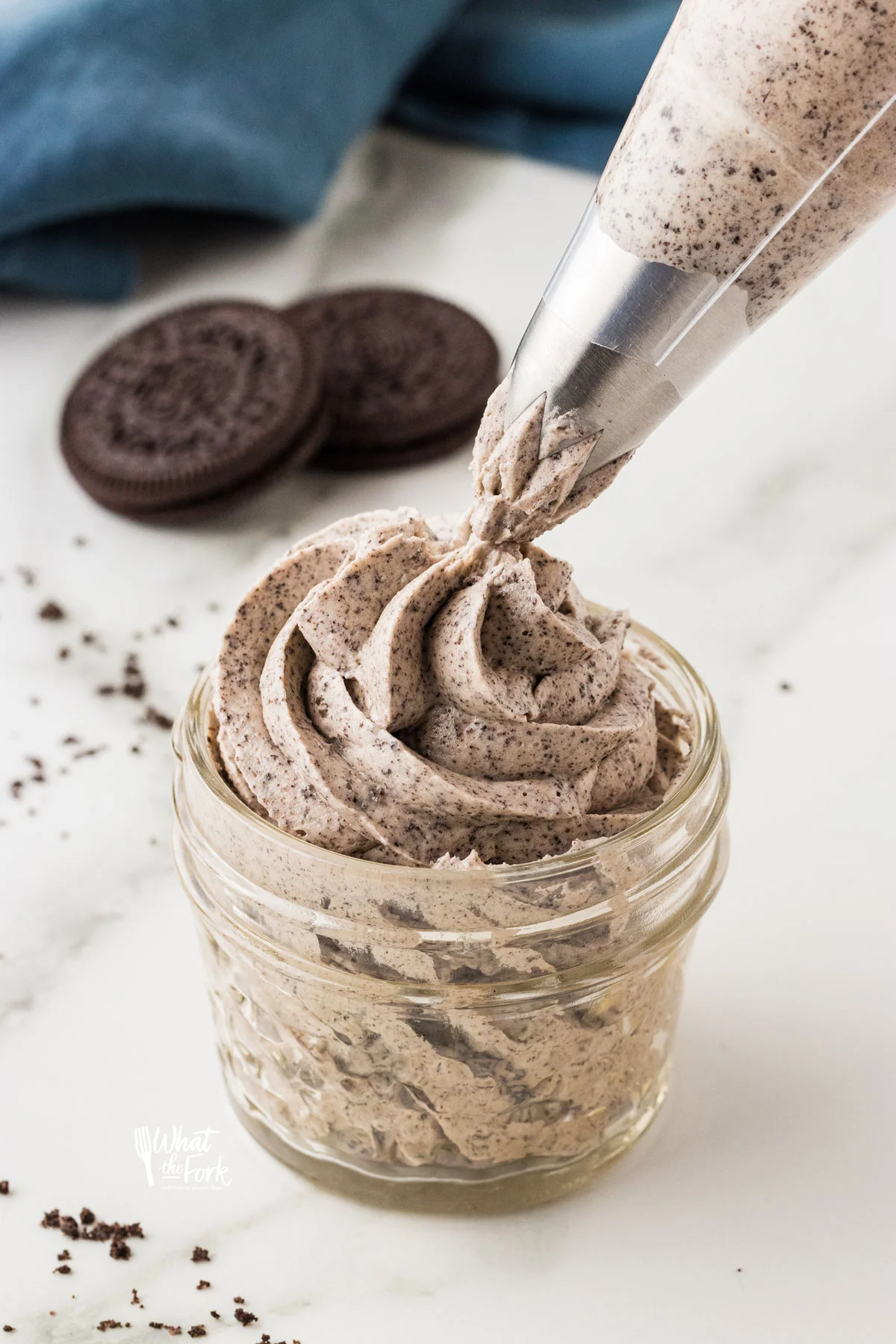 Cookies and Cream Frosting Recipe being piped into a small glass jar with a piping bag fitted with a large open star tip