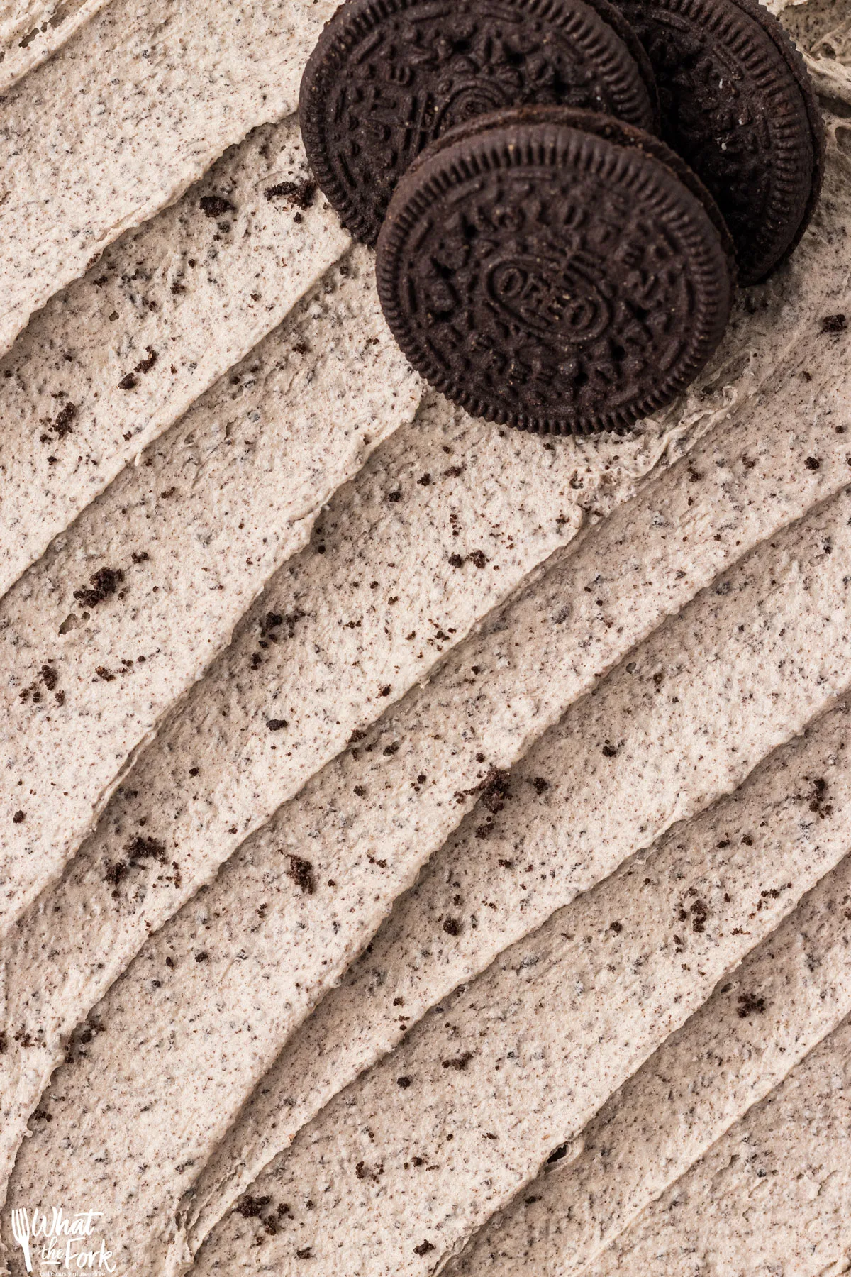 closeup of a Cookies and Cream Frosting Recipe spread on a flat surface with 3 gluten free Oreos in the upper right corner