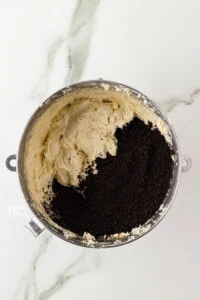 vanilla buttercream frosting in a large silver bowl with crushed gluten free Oreo crumbs to make a Cookies and Cream Frosting Recipe