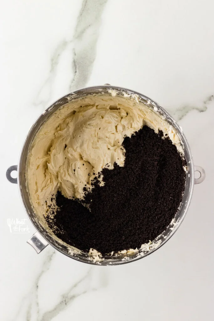 vanilla buttercream frosting in a large silver bowl with crushed gluten free Oreo crumbs to make a Cookies and Cream Frosting Recipe