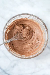 A silver whisk in a large, clear glass bowl with Nutella Whipped Cream