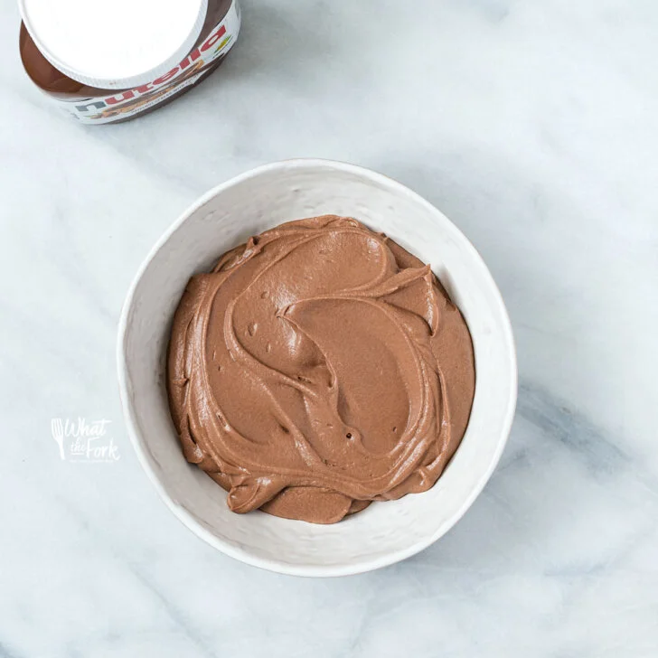 overhead shot of Nutella Whipped Cream in a shallow white bowl with a jar of Nutella in the upper left corner