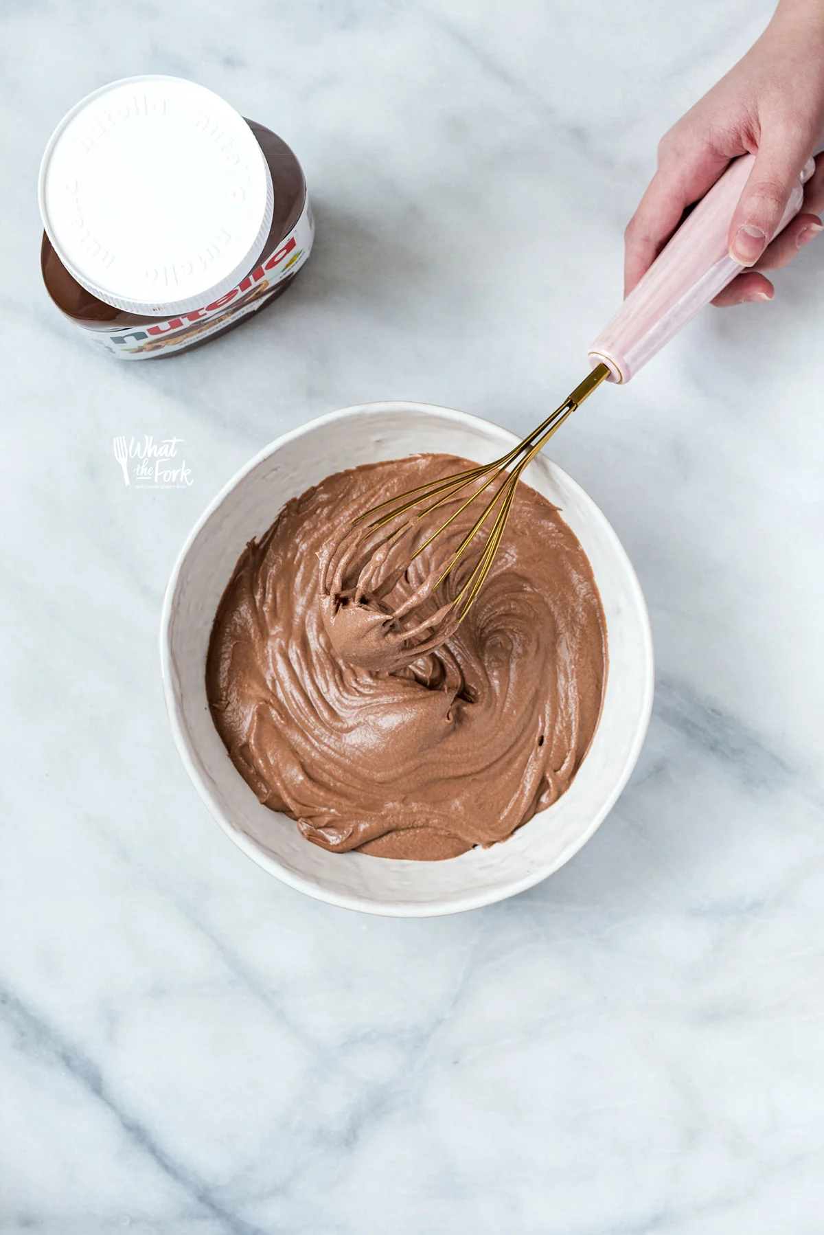 overhead shot of a hand holding a pink and gold whisk in a bowl of Nutella Whipped Cream