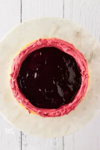 blackberry cake filling in a layer of cake that has a blackberry buttercream dam piped around it