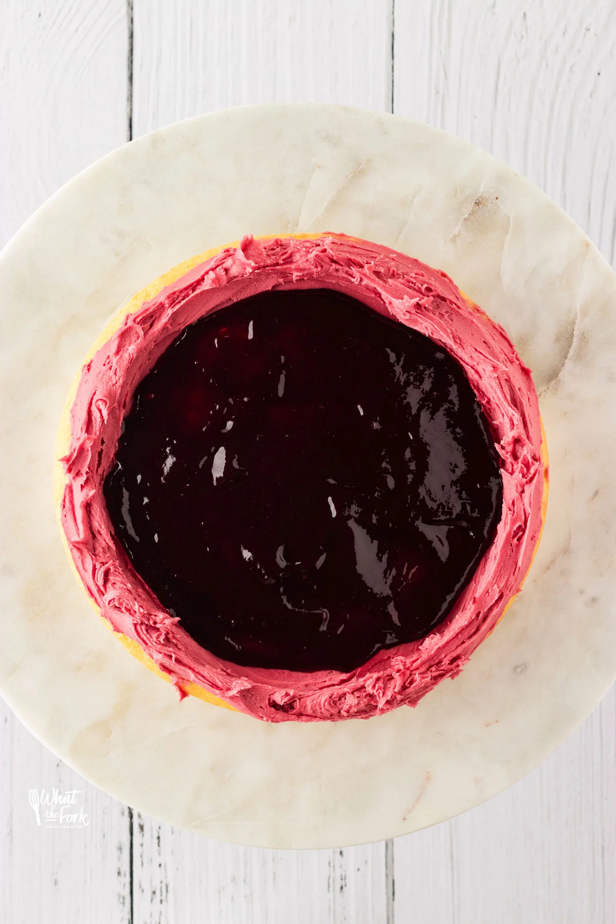 blackberry cake filling in a layer of cake that has a blackberry buttercream dam piped around it