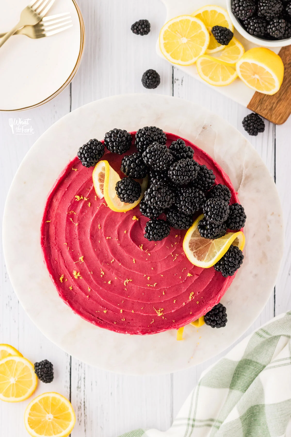 overhead shot of a Gluten Free Lemon Blackberry Cake  on a white cake stand topped with fresh blackberries and twists of lemon.